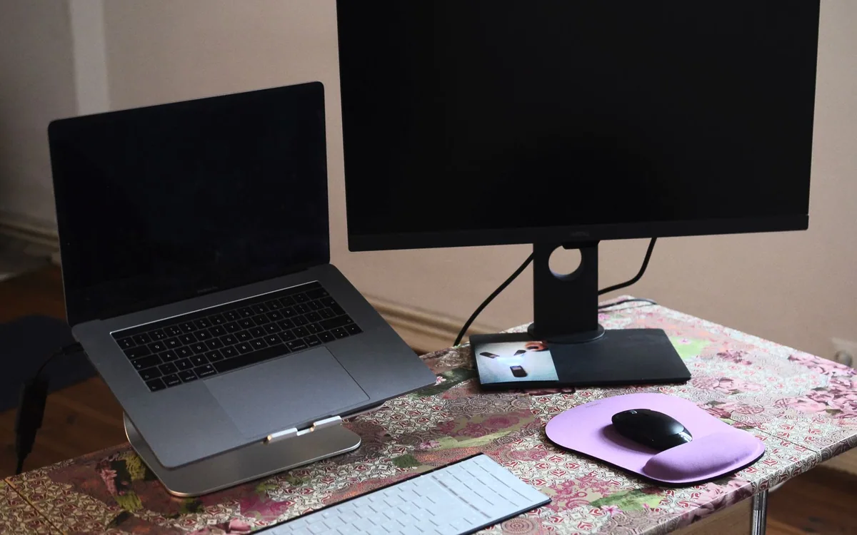 An overhead view of a laptop on a stand beside a monitor, keyboard, and mouse.