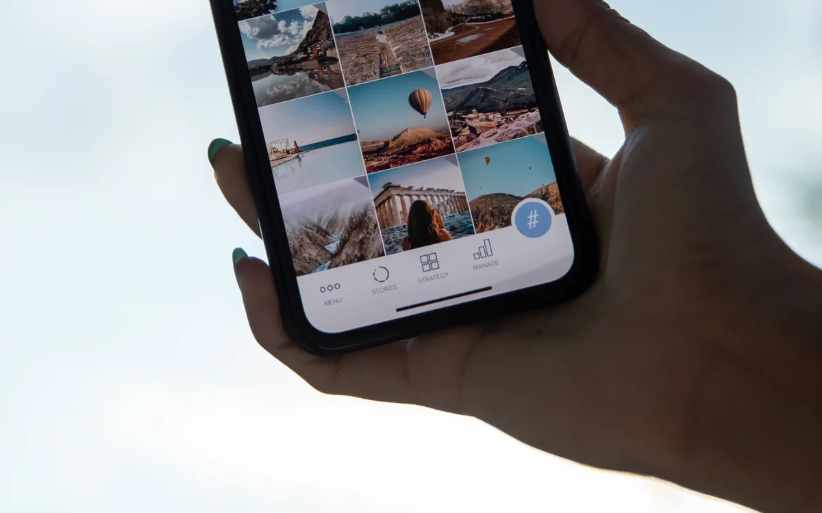A hand holds a smartphone displaying a gallery of travel photographs against the sky.