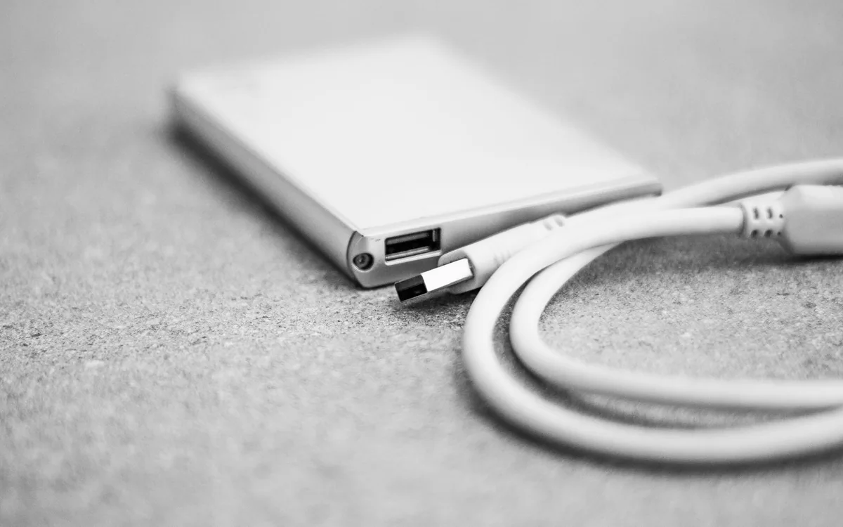 A monochrome close-up of an external storage drive with a USB cable.