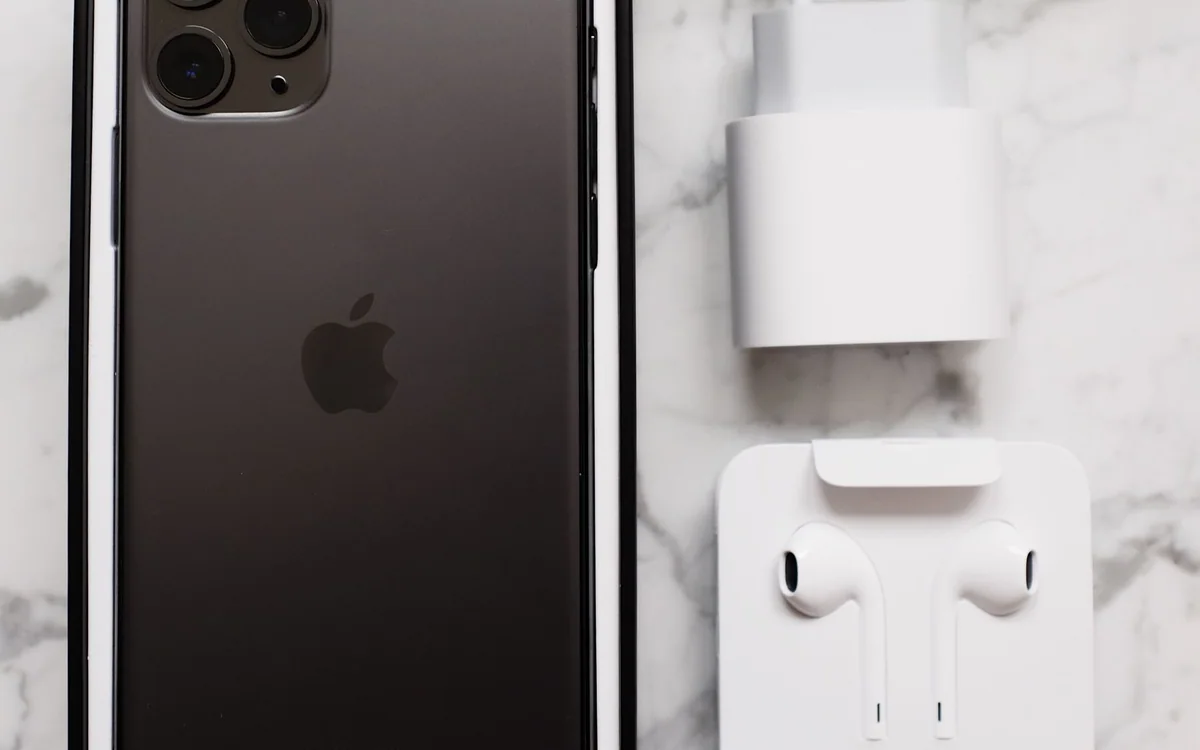 A smartphone in its box is arranged beside earphones, a charger, and cables on a marble table.