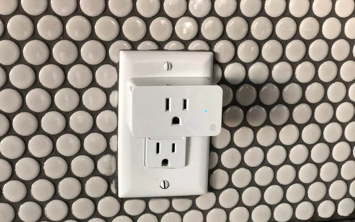 A smart plug installed in a wall socket against a tiled wall.