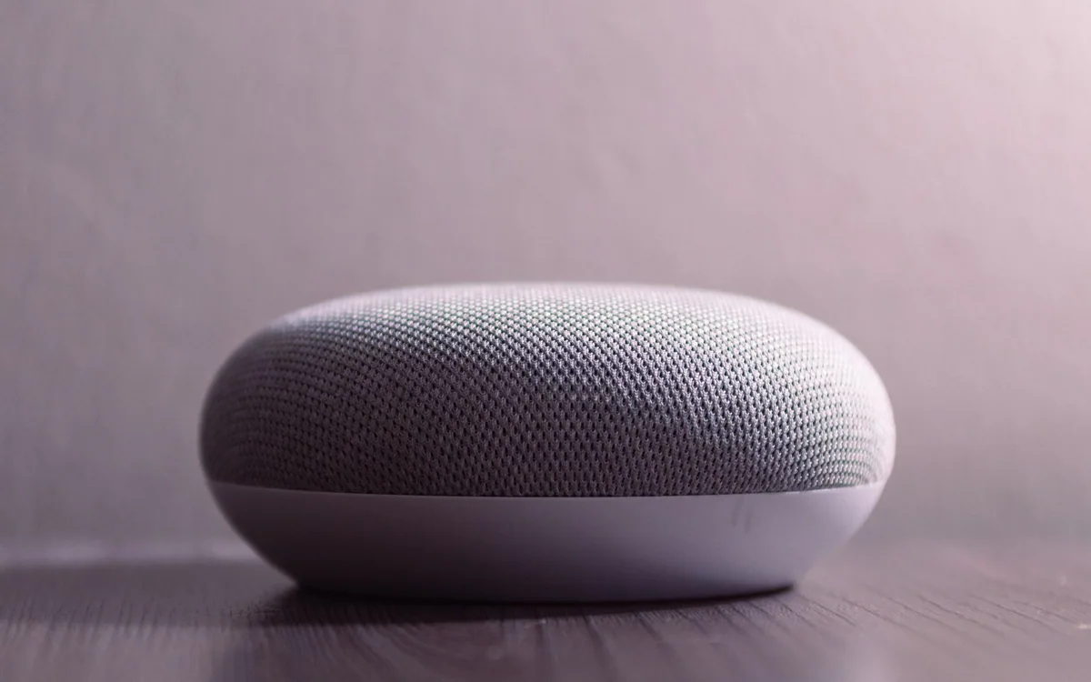 A compact white and gray smart speaker on a wooden table.