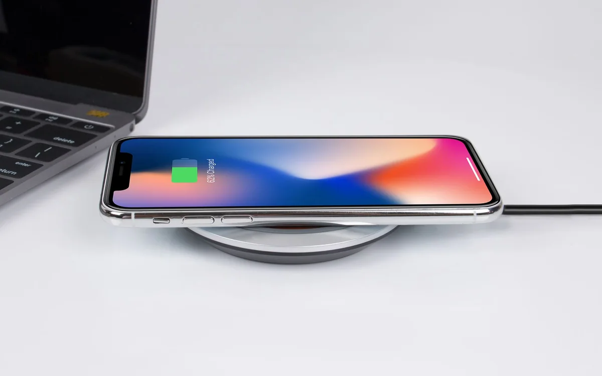 A smartphone rests on a wireless charging pad beside a laptop.